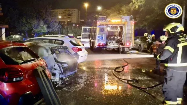 Varios vehículos calcinados en Algeciras y un bombero con manguera echándole agua.