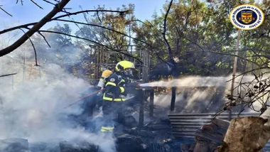 Bombero con manguera, de azul y amarillo, apagando incendio.
