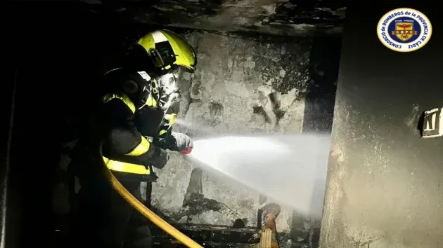 Paredes calcinadas y un bomberos con máscara y manguera apagando el fuego.