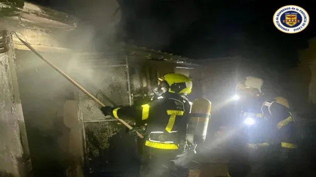 Vivienda con humo y dos bomberos trabajando contra el incendio.