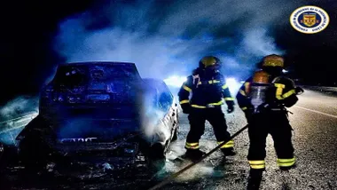 Dos bomberos en la noche apagando las llamas en un vehículo.