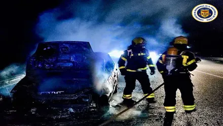 Dos bomberos en la noche apagando las llamas en un vehículo.