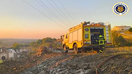 Camión de bomberos amarillo junto a una cuneta calcinada.