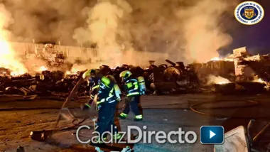 Dos bomberos trabajando y de fondo neumáticos ardiendo.