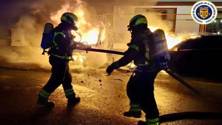 Dos bomberos trabajando en un incendio con las llamas vivas.