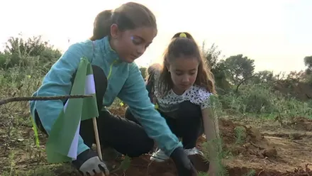 Dos niñas agachadas plantan en la tierra del Parque de Las Canteras, en Puerto Real.