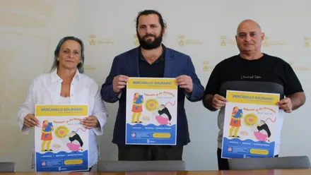 Organizadores del Mercadillo Solidario en Chiclana posando con el cartel del evento.