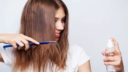 Mujer de pelo castaño se peina y con la otra mano pulveriza.