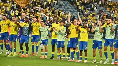 Plantilla del Cádiz CF celebrando sobre el césped junto a la grada del Nuevo Mirandilla tras una victoria reciente. Se aprecia la unión entre jugadores y afición.