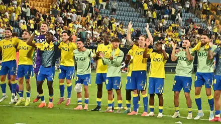 Plantilla del Cádiz CF celebrando sobre el césped junto a la grada del Nuevo Mirandilla tras una victoria reciente. Se aprecia la unión entre jugadores y afición.