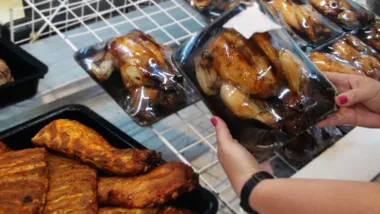 Mujer eligiendo un pollo asado con una bandeja en la mano.
