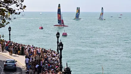 Vista del Paseo de Santa Bárbara en Cádiz lleno de público siguiendo las regatas de la SailGP 2025, con el mar de fondo y los catamaranes compitiendo en el campo de regatas frente a la ciudad.
