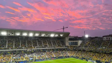 Vista del Estadio Nuevo Mirandilla al atardecer, sobre las gradas de Tribuna y Fondo Norte se ve la luz rojiza del cielo de Cádiz.