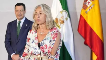 Rocío Hernández en un acto, tras ella Juanma Moreno, destacan las banderas de España y Andalucía.