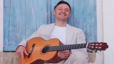 Rufo con su guitarra recostado sobre una pared en color celeste.