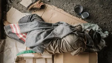 Persona durmiendo sobre cartones tapado con una manta gris.