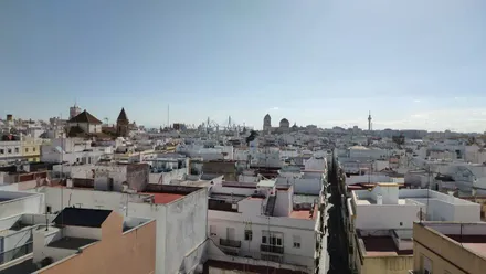 Vista panorámica de Cádiz desde una azotea, con la Torre Tavira, la Catedral y el Pirulí en primer término, y el segundo puente al fondo bajo un cielo azul despejado.