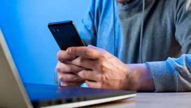Hombre manipulando un teléfono móvil junto a un ordenador portatil.