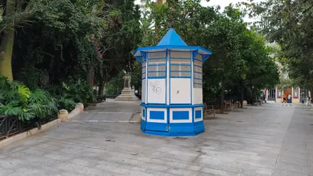 Vista de la Plaza Mina de Cádiz con el kiosco cerrado en primer plano, árboles frondosos y cielo gris claro con nubes altas, en una mañana húmeda de otoño.