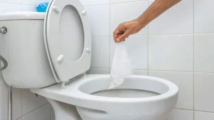 Mano tirando una toallita higiénica en un retrete.