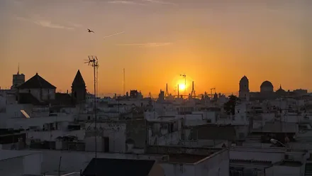 El sol se eleva entre las torres del segundo puente de Cádiz este 17 de octubre mientras se observan recortadas a contraluz las siluetas de la Torre Tavira, la Iglesia de San Lorenzo y la Catedral