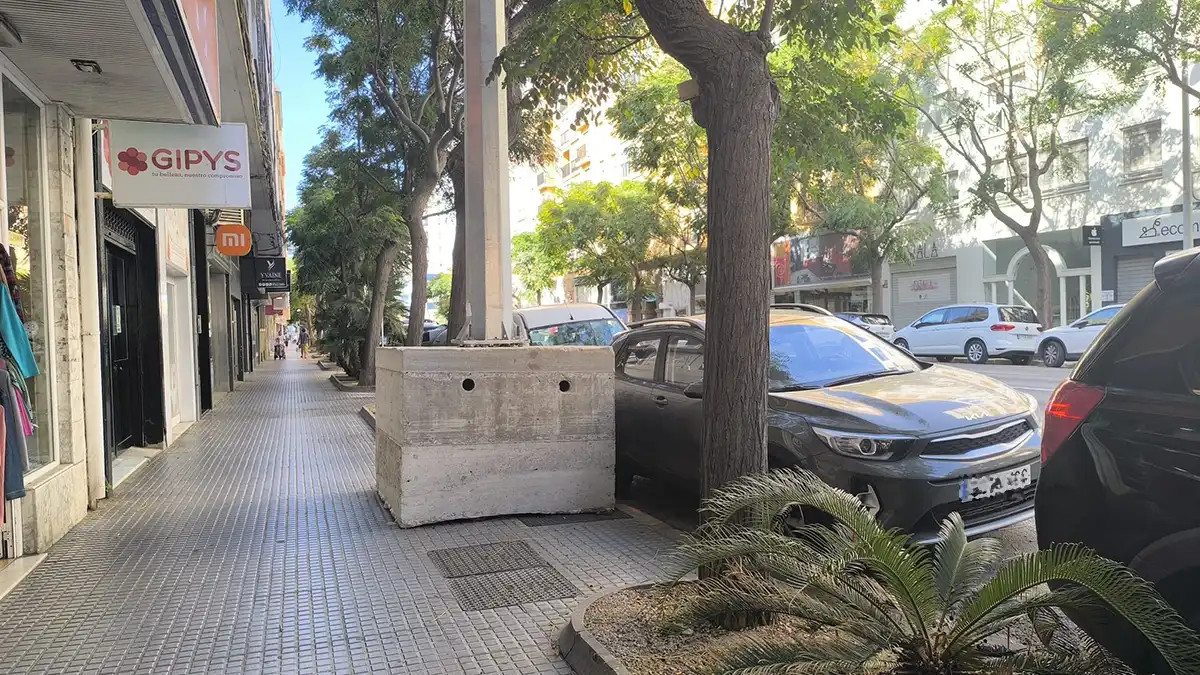Imagen de la Avenida principal de Cádiz con una torreta metálica del alumbrado navideño ya colocada. La estructura se eleva sobre dos bloques de hormigón gris en mitad del acerado, con tráfico y edificios residenciales al fondo en una escena diurna.