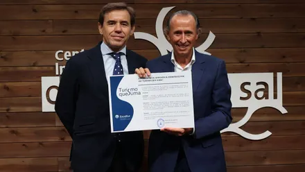 Óscar Perelli y José María Román en el acto, sostiene el título de "Turismo que suma".