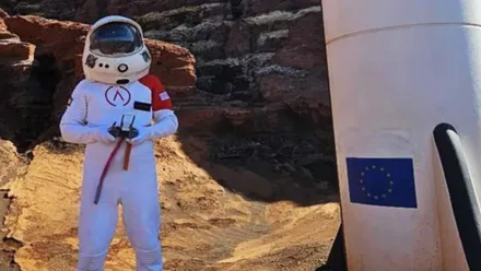Hombre vestido de astronauta y cohete a su lado.