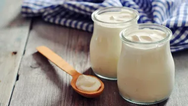 Dos envases de cristal de yogurt natural con una cuchara de madera a su lado.