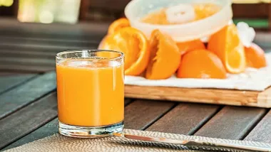 Un vaso con zumo de naranja y detrás un exprimidor con restos de las mismas.