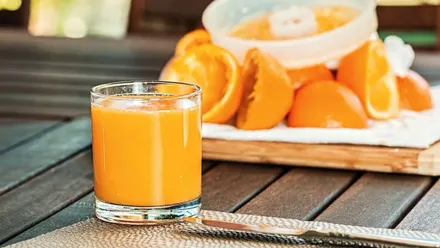 Un vaso con zumo de naranja y detrás un exprimidor con restos de las mismas.