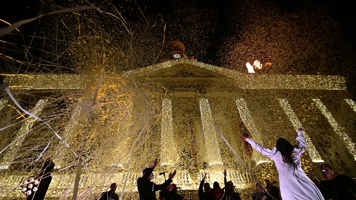 La fachada del Ayuntamiento de Cadiz con la iluminacion extraordinaria de Navidad encendida mienytras caen papelillos y serpentinas y la bailaora María Moreno y su grupo están en el escenario.