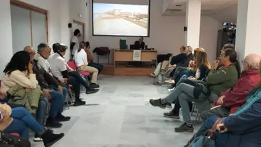 Personas asistentes a la Asamblea del Clima de Puerto Real, es una habitación amplia y destaca la pantalla al fondo.