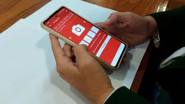 Manos sosteniendo un móvil con pantalla roja y blanca con la aplicación de avisos ciudadanos en Chiclana.
