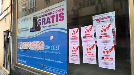Fachada de una copistería low cost en Cádiz completamente cubierta por carteles blancos con el lema “Boicot a la low cost”.