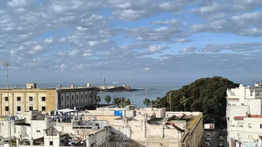 La Caleta recupera la calma este miércoles, con nubes sueltas y amplios claros sobre el Castillo de San Sebastián, visto desde la azotea de Valcárcel. Al fondo, un buque militar navega tras la fortaleza.