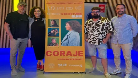 Director y equipo junto al cartel de "Coraje" en tonos anaranjados.