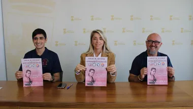 Organizadores sosteniendo un cartel de tonos rosas, en sus manos, del Curso de Defensa en Chiclana.