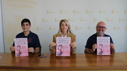 Organizadores sosteniendo un cartel de tonos rosas, en sus manos, del Curso de Defensa en Chiclana.