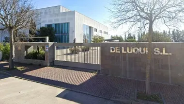 Puerta e instalaciones de De Luque S.L., muro en gris y edificio en blanco.