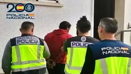 La Policía conduce al detenido al interior de comisaría, porta chaleco rojo.