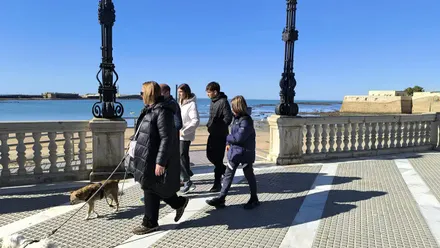 Una familia pasea en un día fresco con sus perros por la zona superior de la Playa de la Caleta de Cádiz, que se ve al fondo.