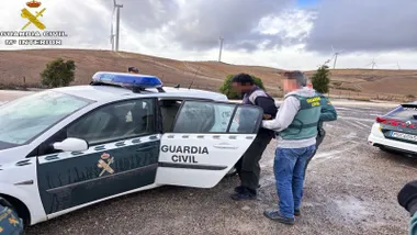 Un Guardia Civil mete en el coche al detenido esposado.