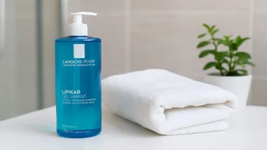 Gel de ducha en un envase celeste junto a una toalla.