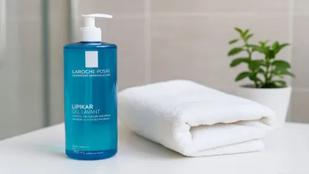 Gel de ducha en un envase celeste junto a una toalla.