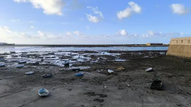 Impresionante bajamar en la playa de la Caleta en una mañana despejada de noviembre, con barquitas sobre las rocas y dos hombres trabajando en dos de ellas.