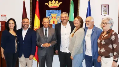 Fuerzas municipales y el pregonero Julio Aragón posando junto al escudo de Chiclana y banderas institucionales.