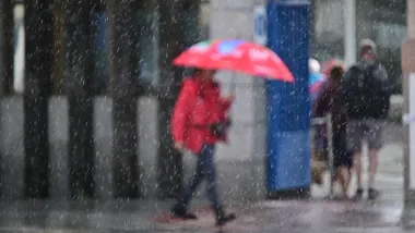 Una mujer caminando bajo la lluvia con un paraguas, captada durante la borrasca Claudia; se aprecian las gotas de lluvia en el aire y el suelo mojado
