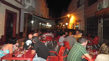 Personas sentadas en los bares de la calle Las Corte del San Fernando en unas sillas rojas.