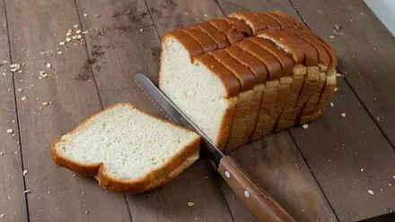 Pieza de pan de molde y un cuchillo cortando una rebanada.